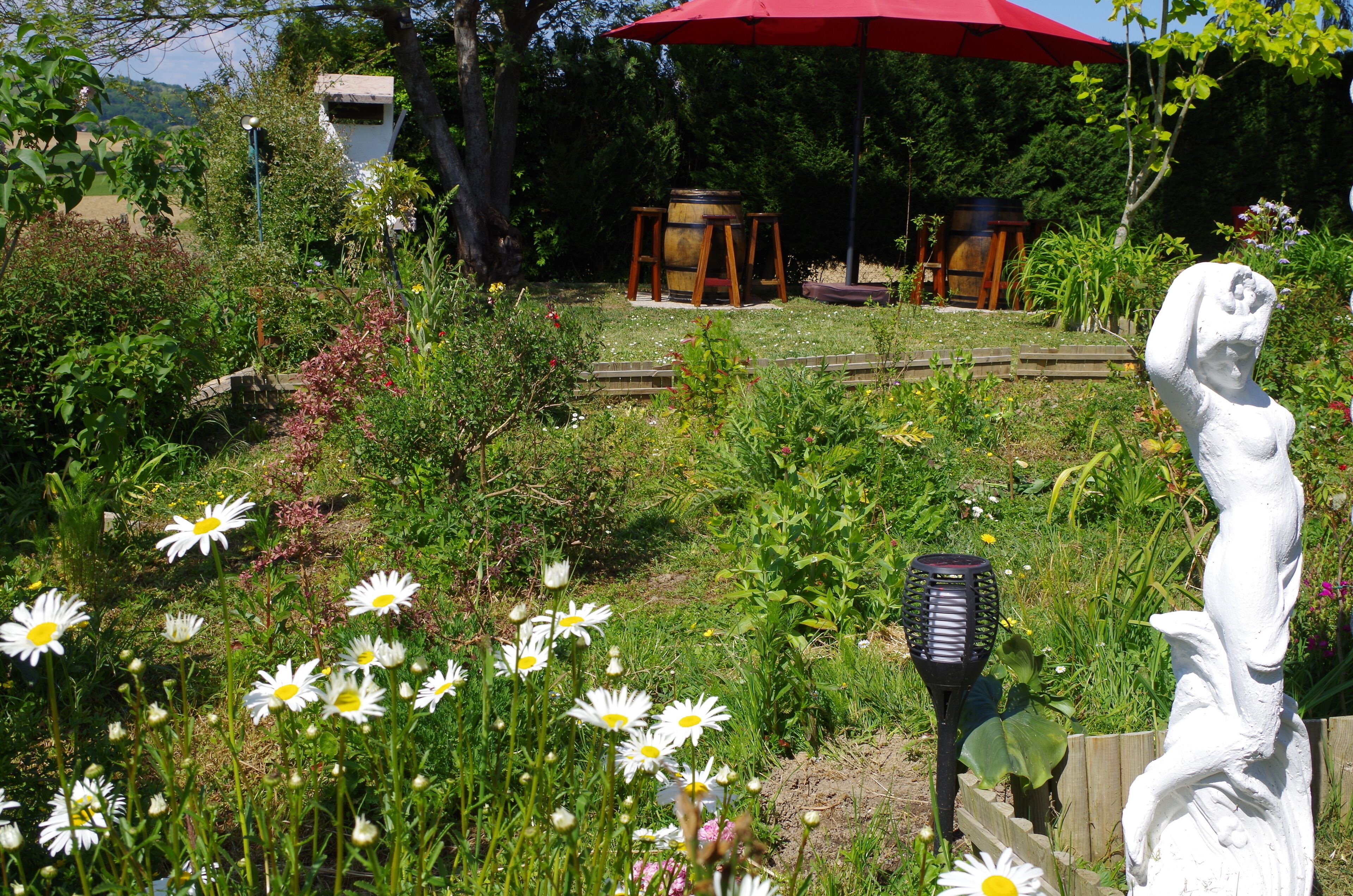 Un jardin avec une statue, un parasol rouge et une table en bois.