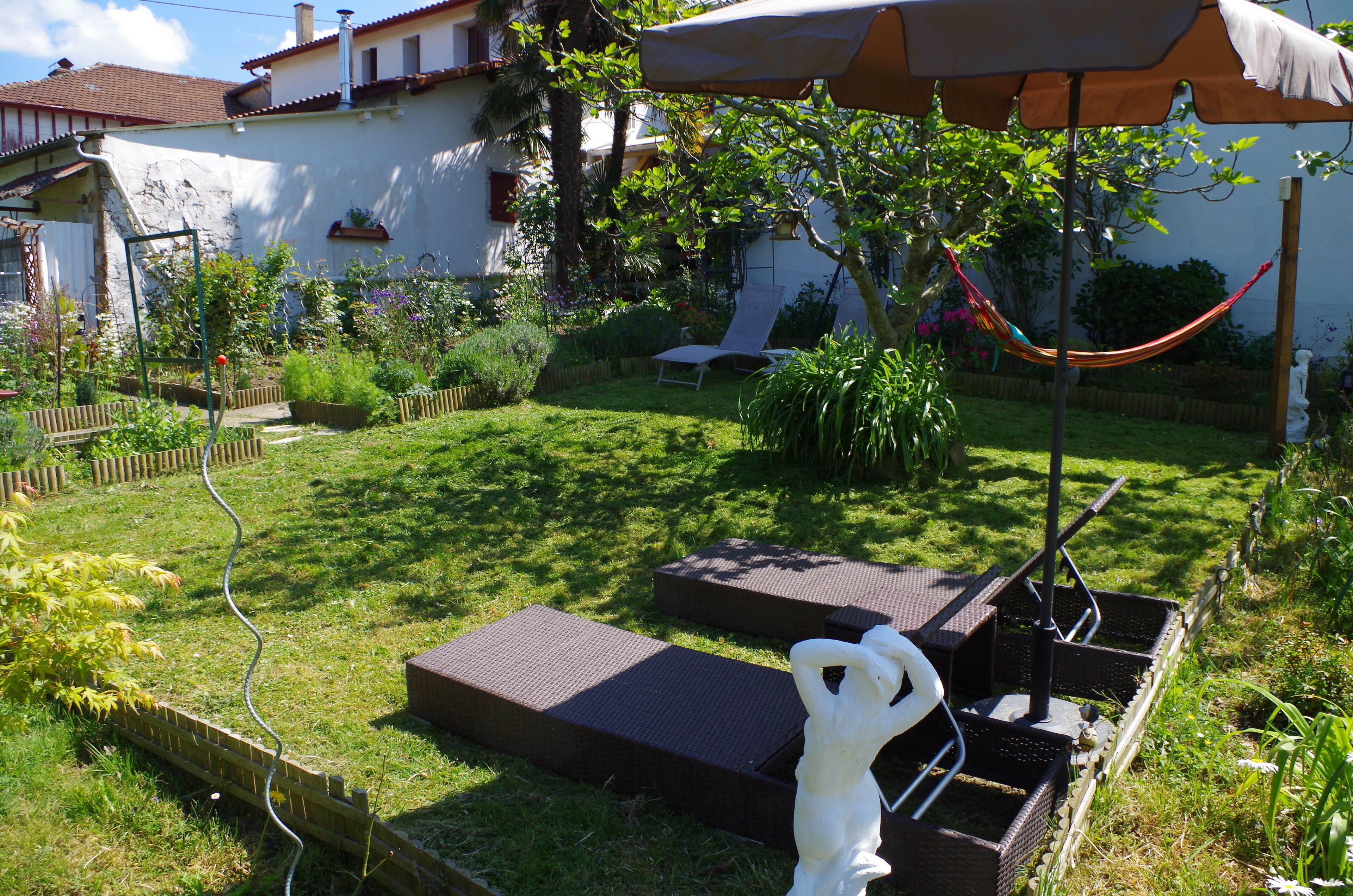 Un jardín con una hamaca, una estatua y mobiliario de exterior.