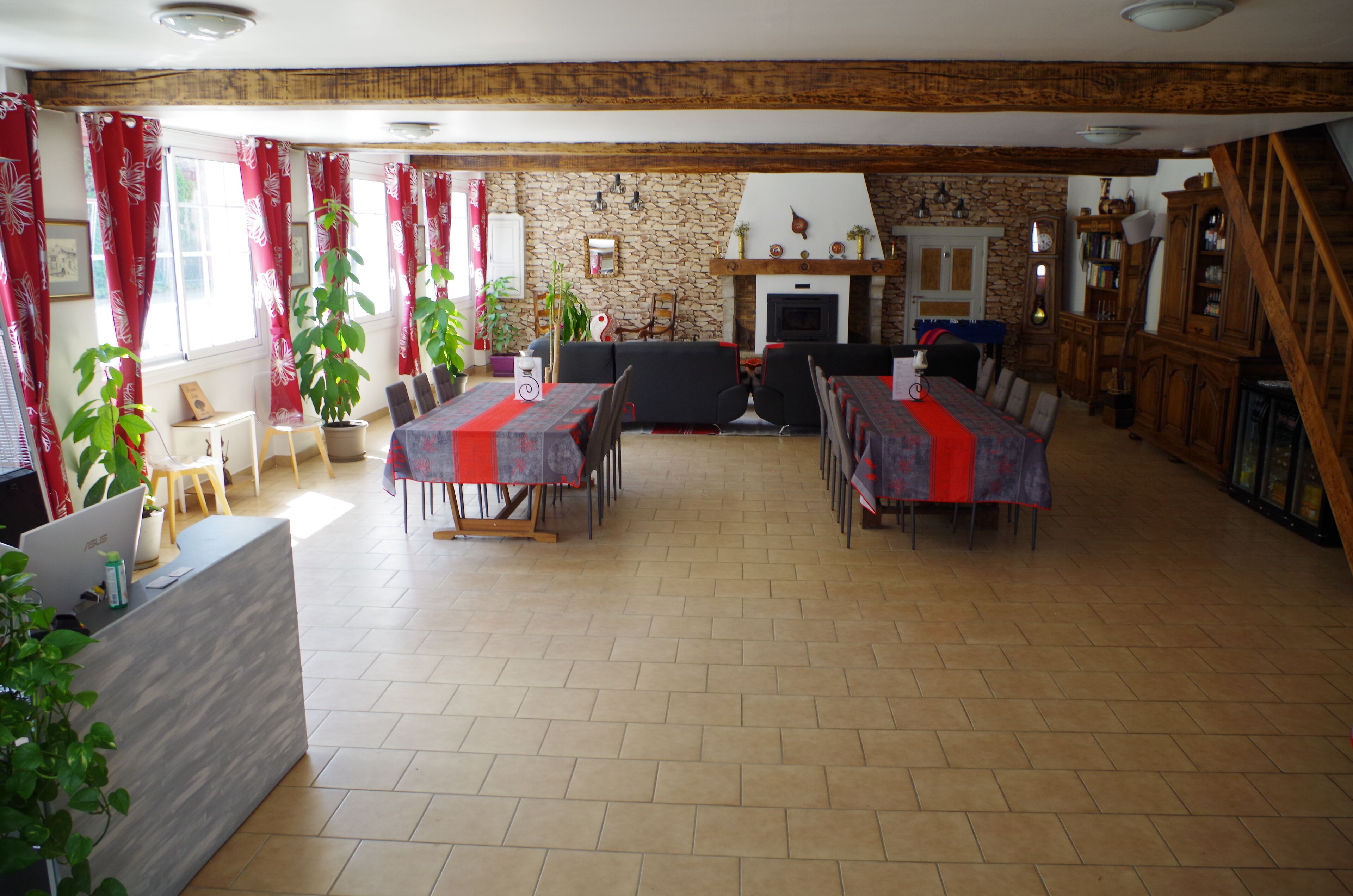 A dining area with a stone wall, wooden beams, and a fireplace. Tables are set with red tablecloths.