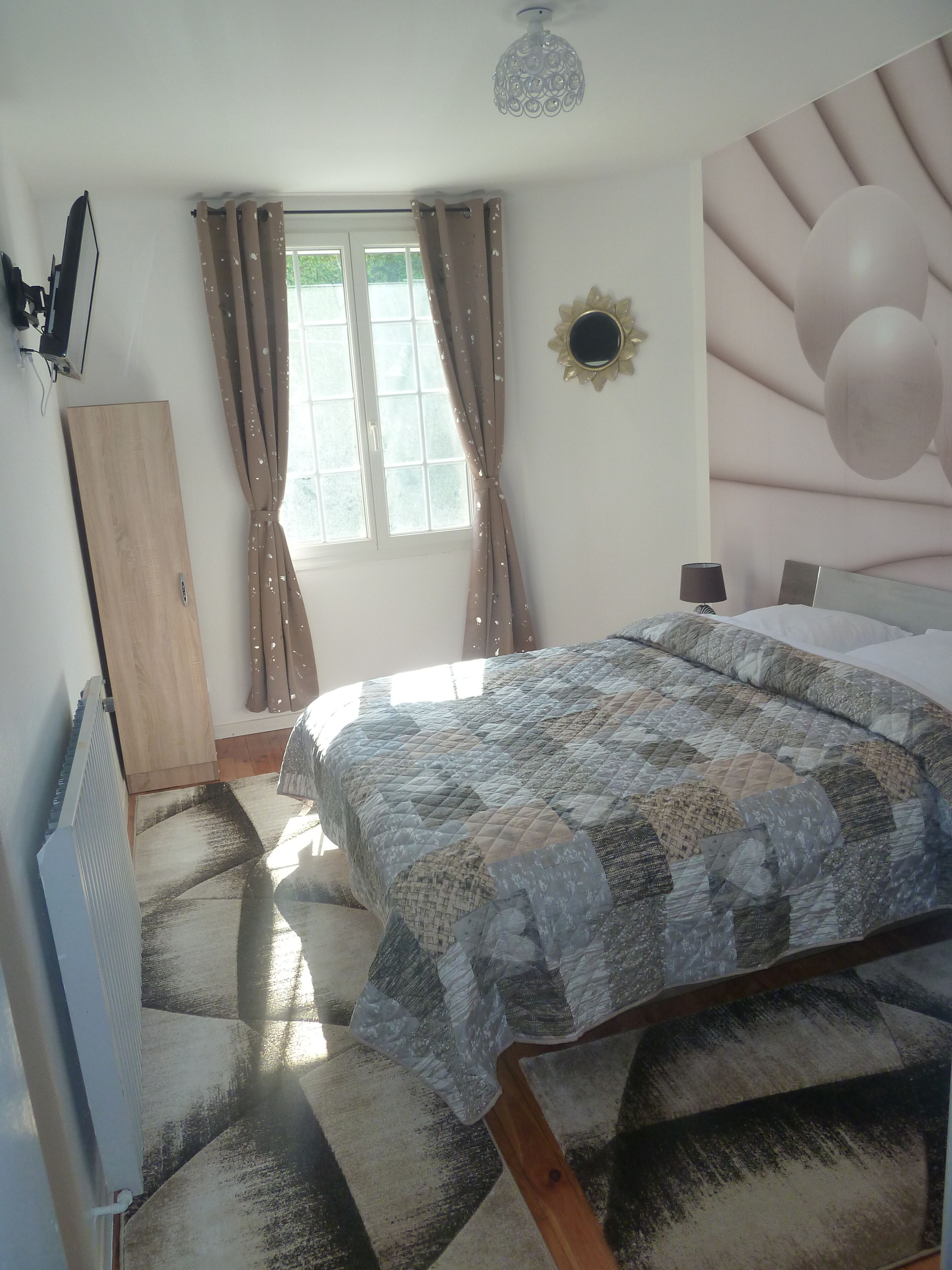 Een slaapkamer met een bed, een radiator, een raam met gordijnen, een spiegel aan de wand en een plafondlamp.
