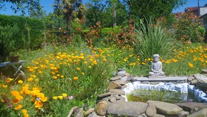 A garden with a Buddha statue, a pond, and various flowers. - Maison Elizondoa (Masparraute)