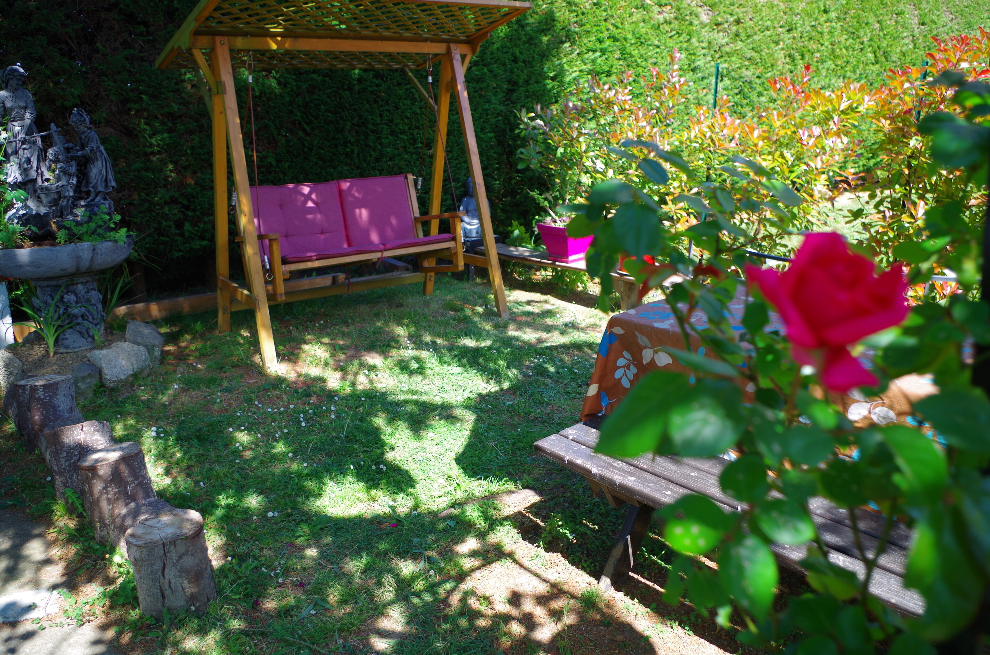 Un jardín con una mecedora de madera, una estatua y un banco.