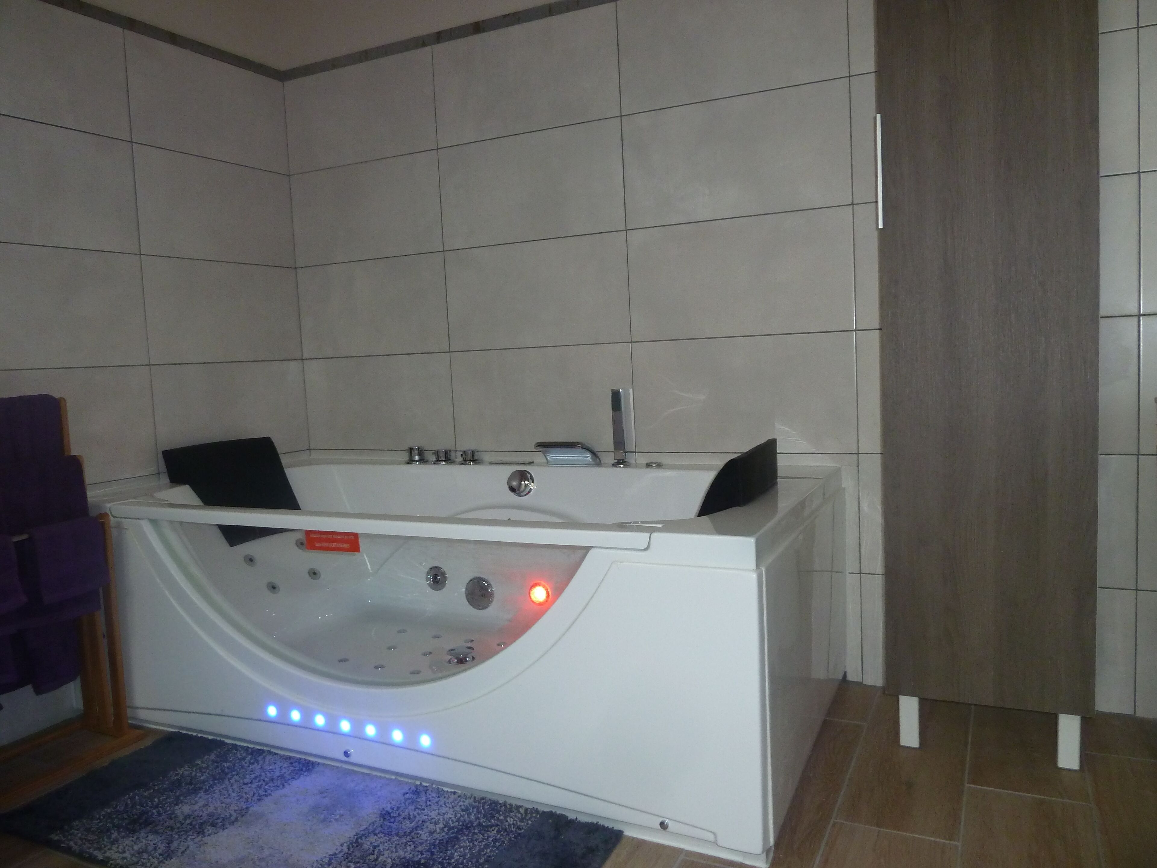 Une salle de bain moderne avec une baignoire blanche, une porte en bois et une serviette violette.