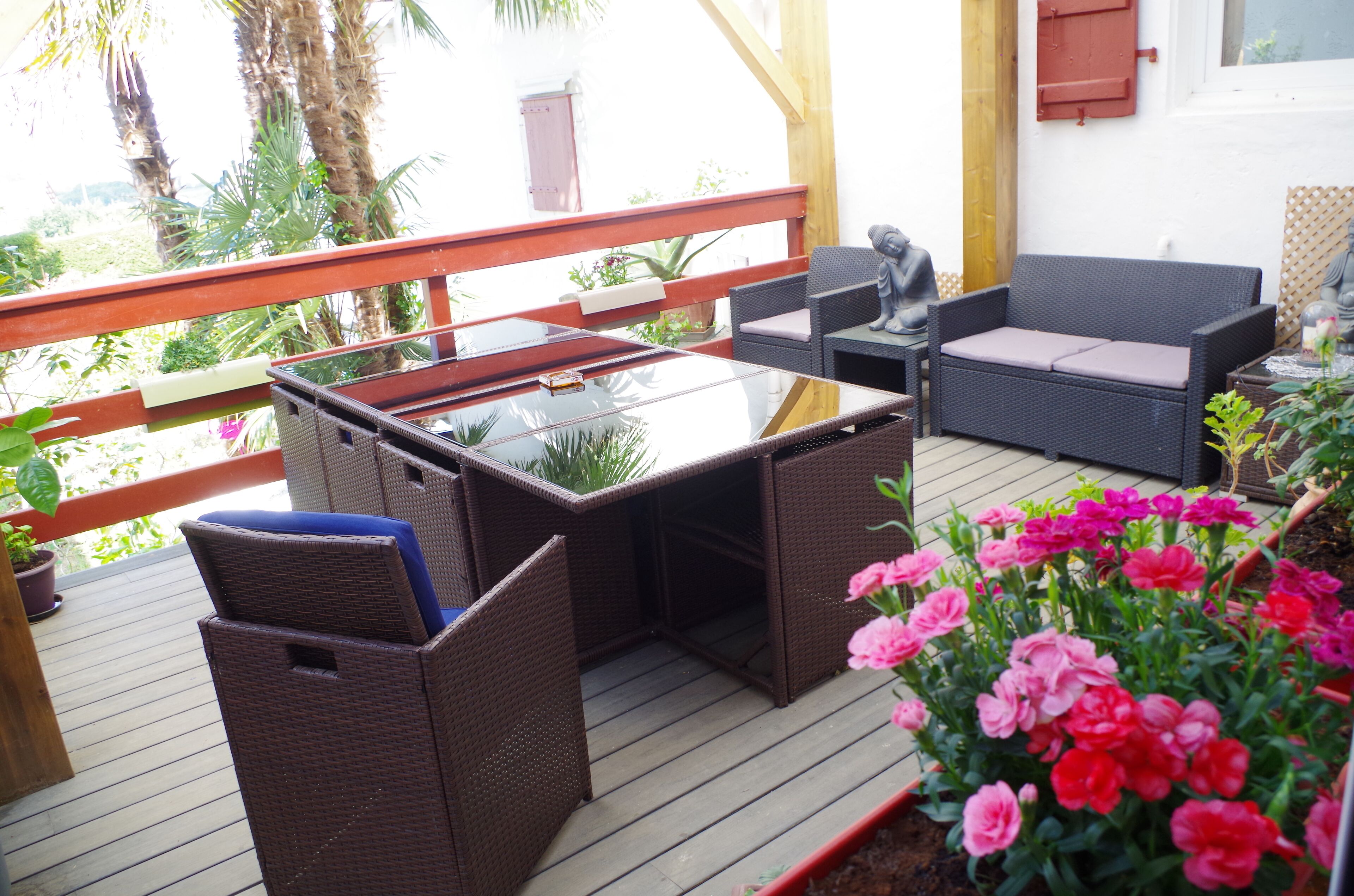 Eine Terrasse im Freien mit Korbmöbeln, einem Glastisch und einer Couch.