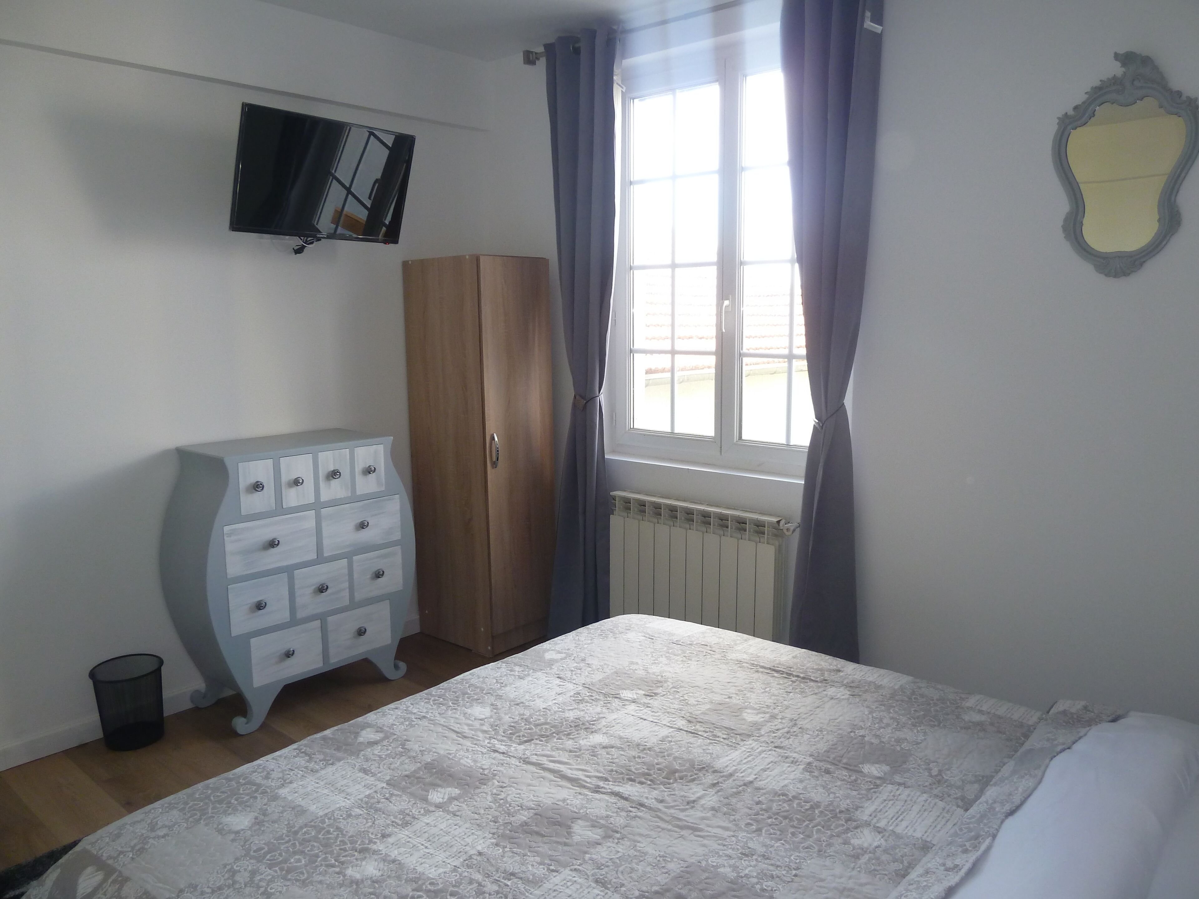 Un dormitorio con cama, armario, radiador, televisor y ventana con cortinas.