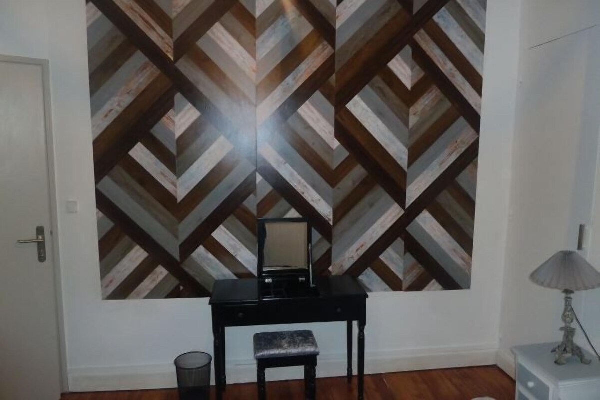 A room with a chevron-patterned wall, a black desk with a chair, a lamp, and a trash can.