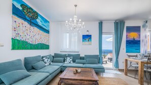 A living room with a large sectional sofa, a wooden coffee table, and a view of the sea through a balcony.