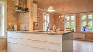 A modern kitchen with a large island, wooden walls, and a chandelier. - Beautiful home in Hebnes with house sea view (Hebnes)