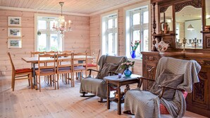 A cozy room with wooden walls and floors, a dining table with chairs, a sofa, and a cabinet with a mirror. - Beautiful home in Hebnes with house sea view (Hebnes)