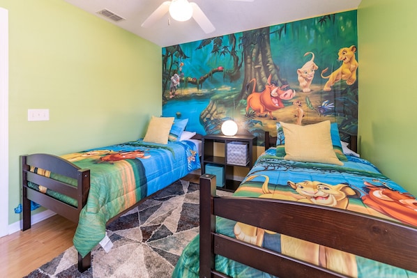 Une chambre dotée de deux lits, chacun recouvert d’une couvre-lit à motifs, d’une table de chevet avec une lampe, et d’une grande fresque murale sur le thème de la jungle.