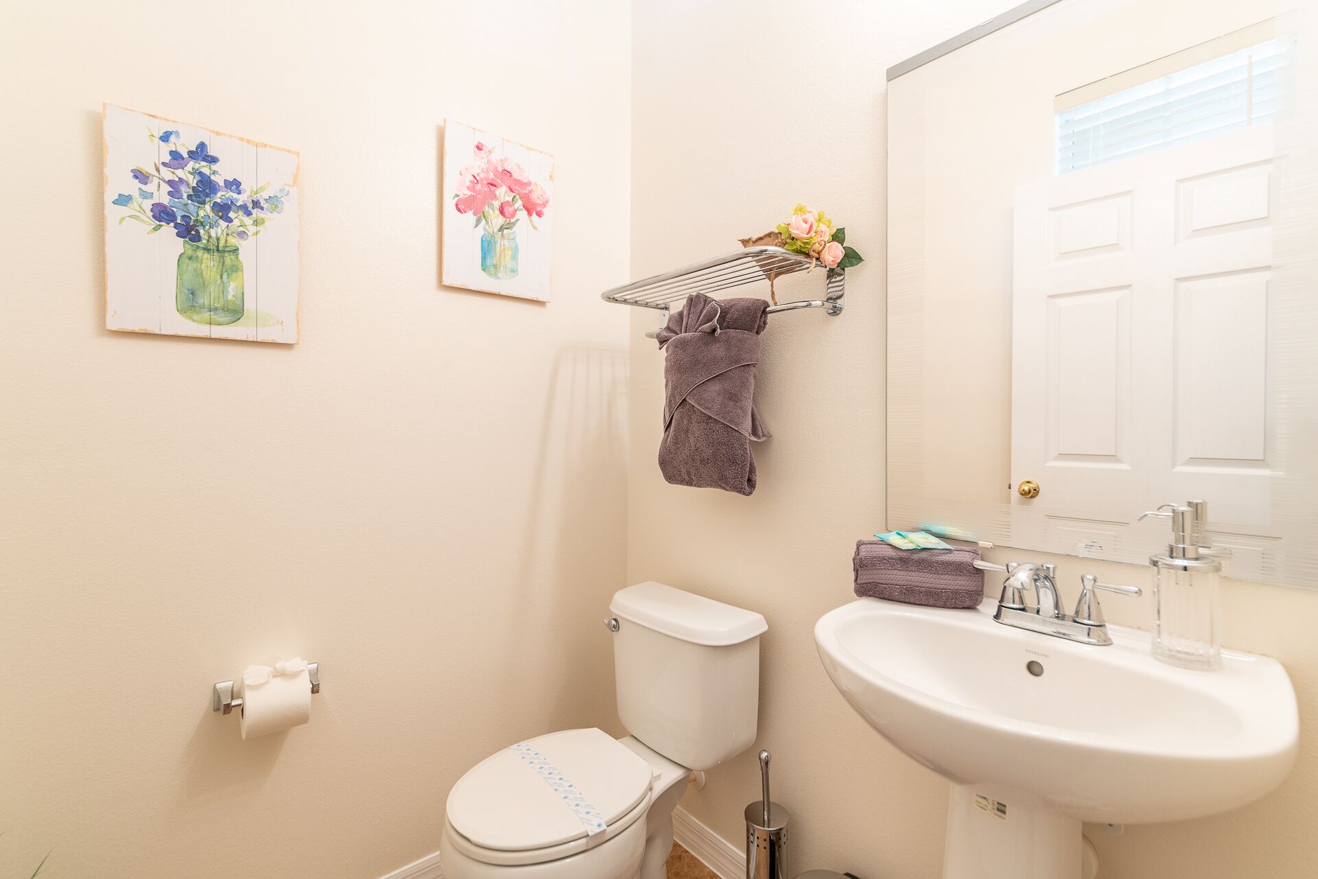 Une salle de bain équipée de toilettes, d’un lavabo et d’un porte-serviettes. Deux tableaux encadrés ornent le mur.