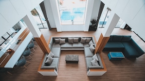 Un vaste espace de vie comprenant un grand canapé d’angle, une table basse et une vue sur une piscine, visible à travers une grande fenêtre.
