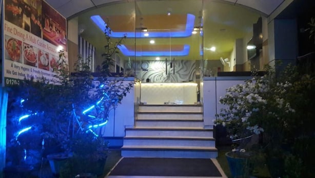 A hotel entrance with a reception desk, a staircase leading to the upper floor, and a signboard advertising a fine dining restaurant. - Hotel Green View Palace (Noida)