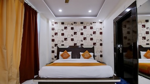A hotel room with a large bed, a headboard with decorative elements, a mirror, and a patterned wall. - Hotel Green View Palace (Noida)