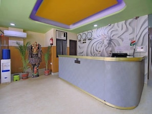 A reception area with a counter, potted plants, a fire extinguisher, and a decorative wall with clocks. - Hotel Green View Palace (Noida)