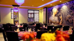 A restaurant with tables set for dining, a chandelier, and a mural on the wall. - Hotel Green View Palace (Noida)
