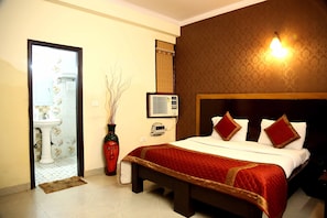A hotel room with a bed, a bedside table, a wall-mounted air conditioner, and a bathroom visible through an open door. - Hotel Green View Palace (Noida)