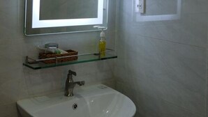 A bathroom with a white sink, a mirror with a light, a glass shelf with toiletries, and a towel rack. - Happy View Hotel (Tan Hai)