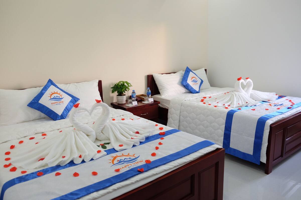 Two hotel beds with white linens, blue accents, and swan-shaped towels.