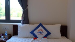 A hotel room with a bed, a wall-mounted light, a window with curtains, and a pillow with a logo. - Happy View Hotel (Tan Hai)