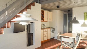 A kitchen with a brick floor, a dining table with chairs, a staircase, and a TV mounted on the wall. - Feriehotel Tranum Klit (Brovst)