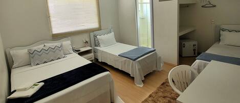 A hotel room with two beds, a small desk, a chair, a heater, and a window with blinds.