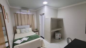 Una habitación de hotel con una cama, una mesita de noche, un calentador, una silla y un armario.