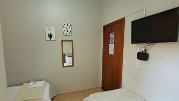 A small, clean room with two single beds, a wooden door, a mounted TV, and a mirror on the wall.