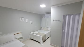 A bedroom with a bed, a bedside table, a chair, a wardrobe, and a shower area.