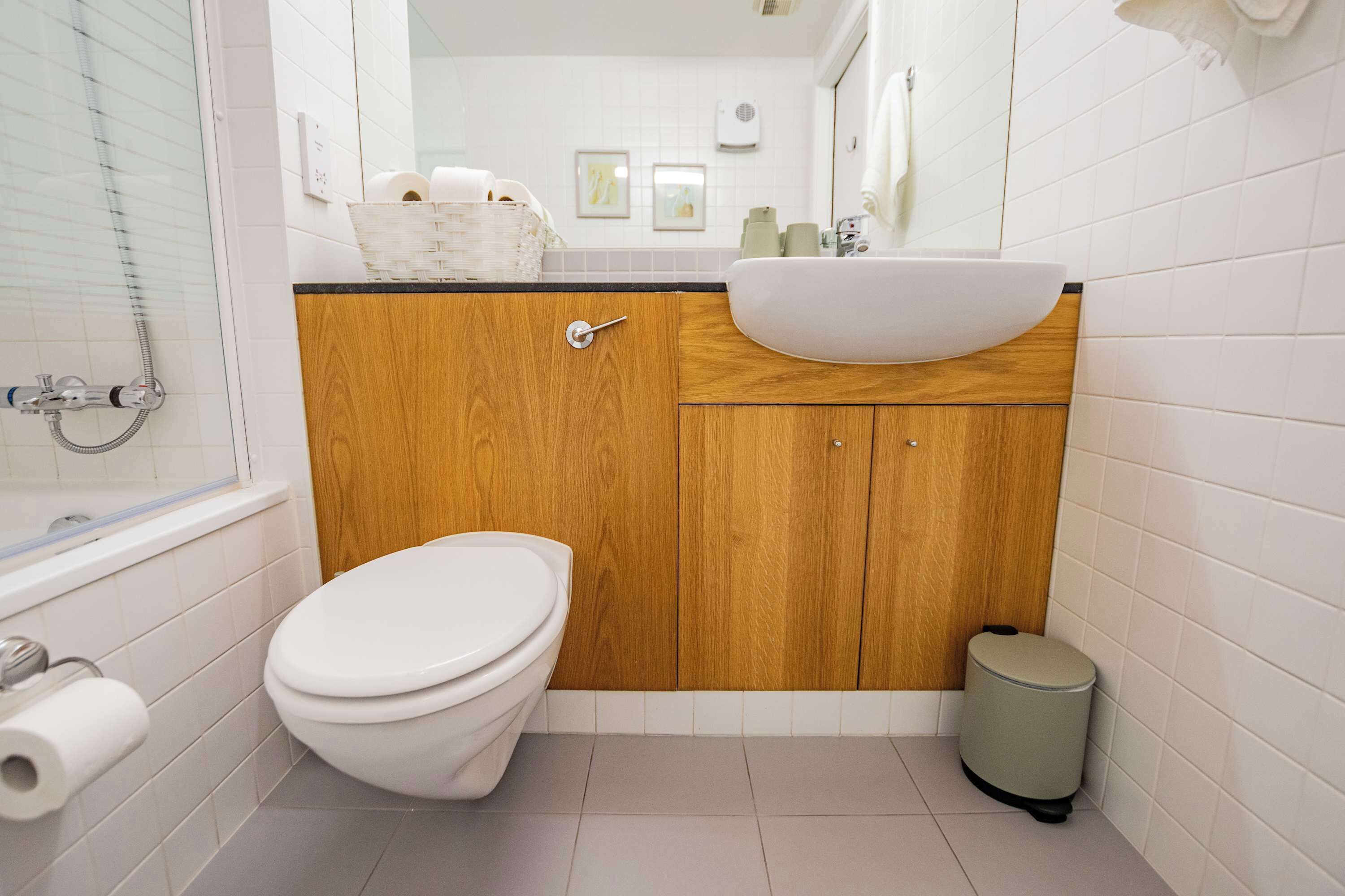 A bathroom with a white toilet, wooden cabinets, a white sink, and a trash bin.