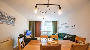 Een moderne woonkamer met een houten eettafel, groene banken en een televisie.