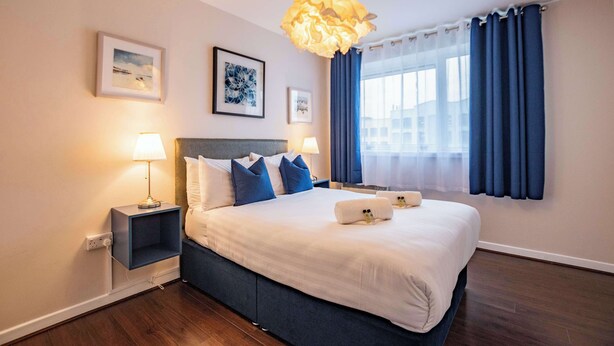 Hotelkamer met een groot bed, twee nachtkastjes, een wandlamp en een raam met gordijnen.