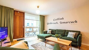 Een gezellige woonkamer met een groene bank, een houten bijzettafeltje en een televisie op een dressoir.