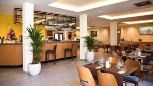 Een modern restaurant met een bar, meerdere eettafels en potplanten.