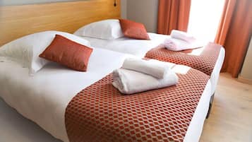 Habitació d'hotel amb dos llits, cadascun amb roba de llit blanca, cobres amb dibuixos vermells i almoades a conjunt.
