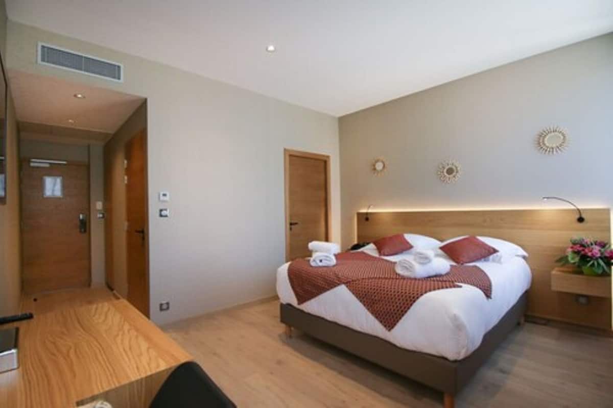 Quarto de hotel moderno com uma cama grande, cabeceira de madeira e uma mesa de cabeceira com abajur.