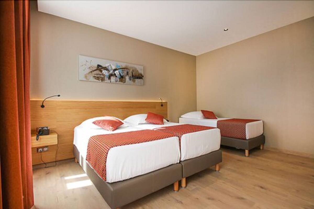 Quarto de hotel com duas camas, uma cabeceira de madeira, uma mesa de cabeceira e um quadro na parede.