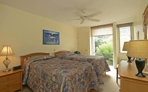 Ein Schlafzimmer mit zwei Betten, einem Deckenventilator, einem Fenster mit Blick auf Grünflächen und einem Gemälde an der Wand.