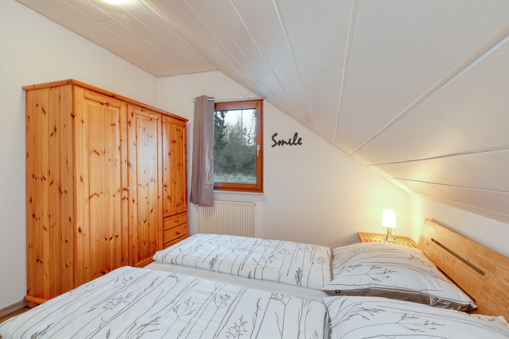 A bedroom with two beds, wooden wardrobe, a window with a view, and a 'Smile' sign on the wall.
