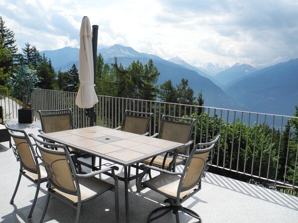 A terrace with a table and chairs, overlooking a mountainous landscape.