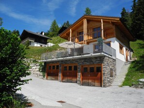 A two-story wooden house with a balcony, stone foundation, and a garage.
