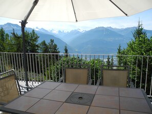 A terrace with a table and chairs, overlooking a mountainous landscape.