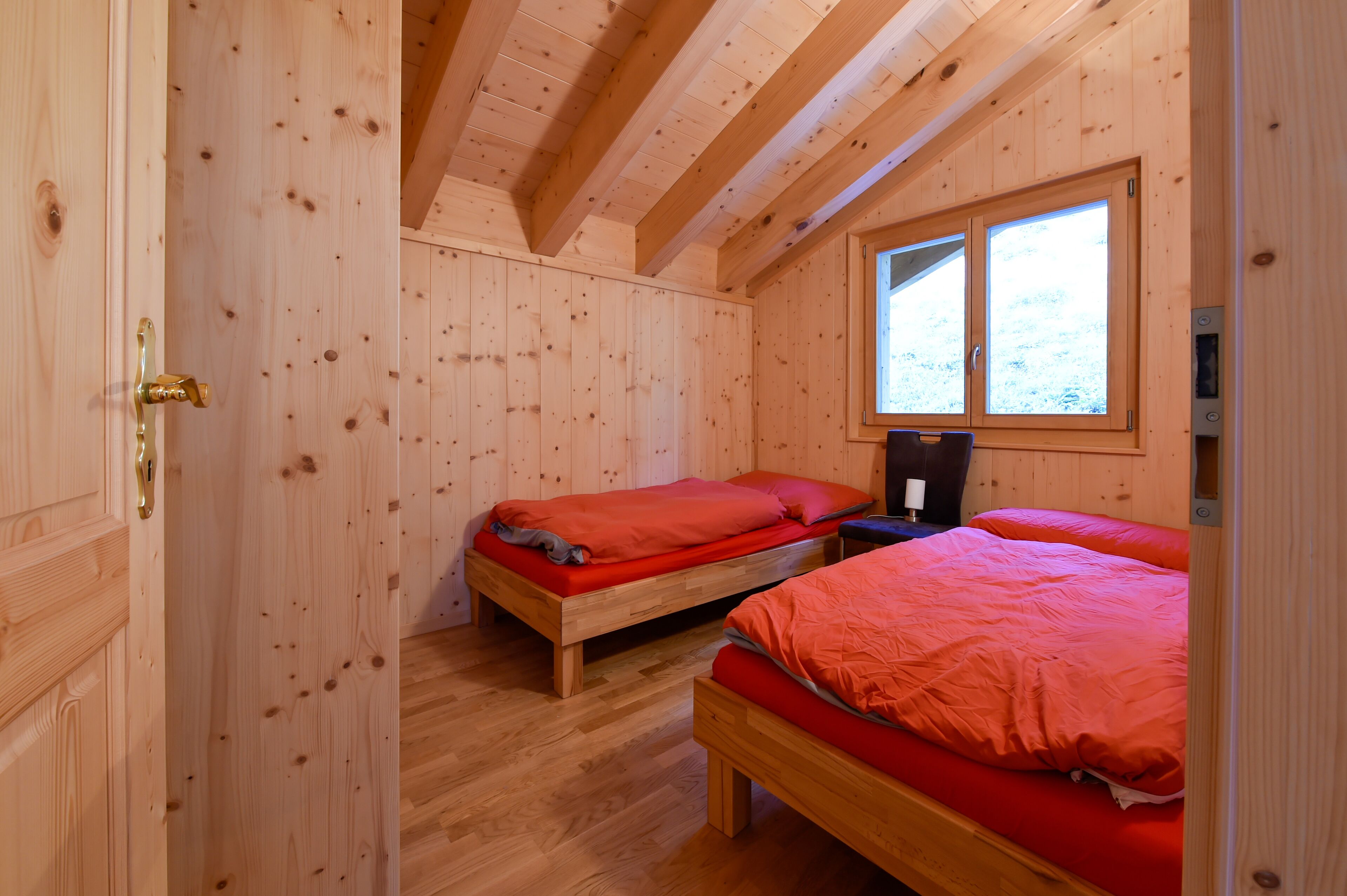 A wooden cabin bedroom with two single beds, a window, and a wooden door.
