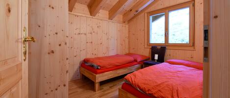 A wooden cabin bedroom with two single beds, a window, and a wooden door.