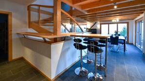 A modern kitchen with a wooden staircase, a bar area with stools, and a dining area with a table and chairs.