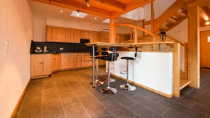 A modern kitchen with wooden cabinets, a central island with stools, and a staircase leading to an upper level.