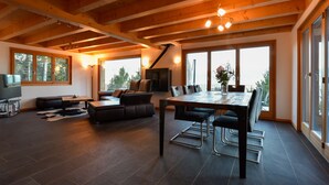 A spacious living area with a wooden ceiling, a large dining table, leather sofas, and a fireplace.