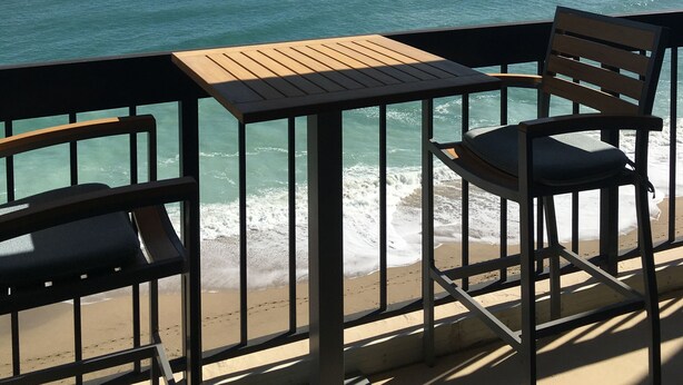 A seaside view from a balcony with a table and two chairs, overlooking the ocean and a sandy beach. - Beach Paradise Found!  Direct oceanfront 9th floor updated and nicely decorated (Jensen Beach)