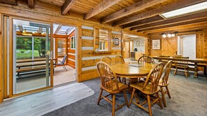 Un intérieur en bois avec une grande table à manger et des chaises, un coin cuisine et de grandes fenêtres.