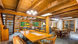 Un intérieur rustique en bois, avec une grande table à manger en bois, des chaises et un canapé dans une pièce chaleureuse dotée d’un haut plafond et de poutres apparentes.
